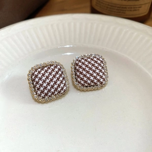 Close-up of golden square earrings with brown houndstooth fabric and zircon borders