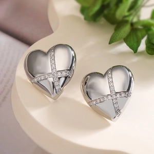 Silver heart-shaped stud earrings with sparkling cross inlay on a soft background