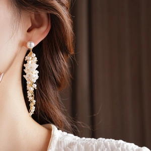 Detail view of long tassel pearl earrings with floral accents worn by a model