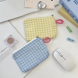 Close-up of yellow and blue plaid zipper pouches with pink pull tabs on a white desk