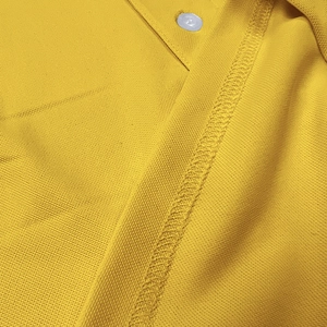 Macro shot of breathable yellow piqué fabric with fine stitching and white button detail