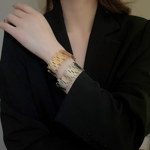 Detail view of gold irregular open cuff bracelets on a black blazer for chic office style