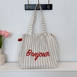 Detail of striped canvas tote bag showing Bonjour embroidery and red drawstring feature