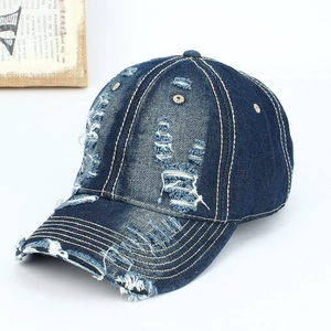 Detailed close-up of distressed blue denim baseball cap with frayed holes and yellow stitching