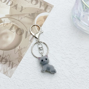 Close-up of grey flocked cat keychain with silver metal lobster clasp and ring on a desk