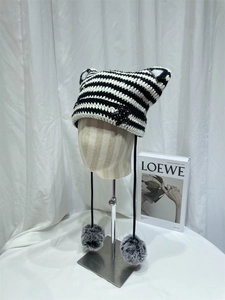 Detail of striped knit cat ear hat featuring star patch and soft faux fur pom-poms