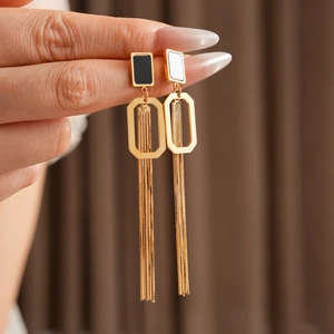 Détail de boucles d'oreilles dorées à pompons avec monture géométrique noir et blanc