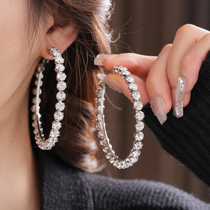 Close-up of model wearing large silver-toned hoop earrings with round sparkling crystals