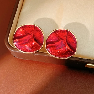 Close-up of red enamel round stud earrings with gold edges and pleated texture on leather