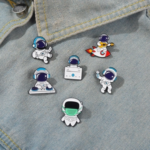 Detailed view of astronaut enamel pins pinned on a blue denim jacket pocket
