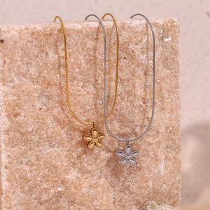 Detail of gold and silver flower pendant necklaces with sleek snake chains on stones