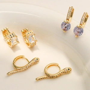 Three pairs of gold-plated geometric earrings with zircon stones on a white ceramic plate
