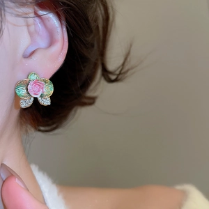 Close-up of pink flower earrings with green enamel leaves and sparkling crystals