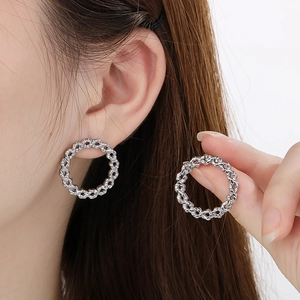 Detail view of silver woven hollow hoop earrings on a model showing high-end texture