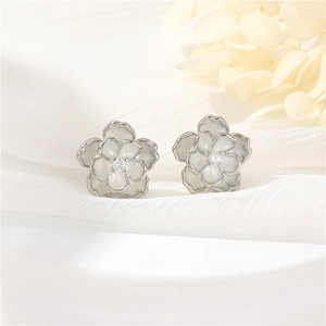 Detail of camellia stud earrings with white enamel petals and central zircon on soft gauze