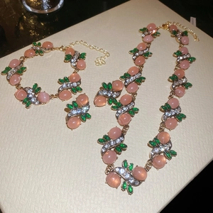 Close-up of elegant jewelry set with pink resin beads and green stones on a gold base