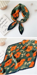 Macro detail of dark green pleated silk scarf featuring vibrant orange floral patterns