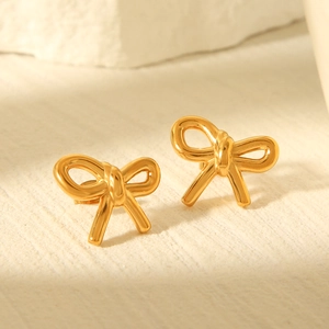 Elegant 18k gold plated bow stud earrings made of stainless steel on a beige background