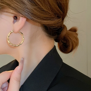Detail view of a gold geometric earring with irregular texture worn by a model