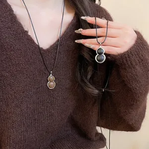 Modern leather gourd pendant necklaces on a model wearing a brown knit sweater
