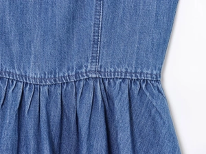 Dettaglio di un abito in denim blu con pieghe in vita e cuciture a contrasto