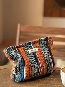 Detailansicht der böhmisch gestreiften Strick-Clutch mit Etikett auf dem Holztisch