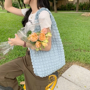 Outdoor lifestyle shot of a light blue puff bubble shoulder bag with a textured finish