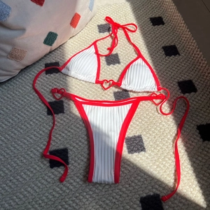 White ribbed bikini set with red trim and heart shaped rings on a textured background