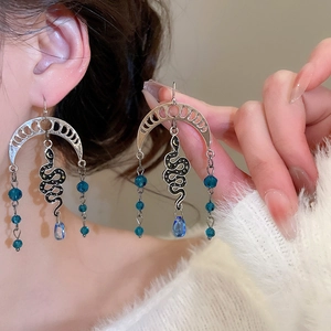 Detailed view of silver snake drop earrings with moon motifs and blue crystal beads