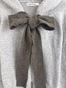Detail of grey knitted hoodie featuring a large dark brown bow and smooth zipper closure
