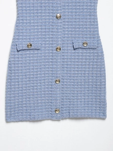 Close-up of light blue tweed fabric texture with decorative gold buttons on pockets