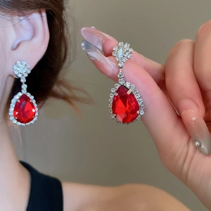 Close-up of sparkling red teardrop earrings with halo diamonds and floral silver studs