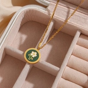 Close-up of 18K gold plated necklace with green enamel flower pendant in a pink jewelry box