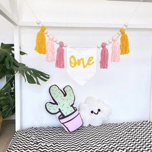 Detail of baby birthday banner with pastel tassels and wooden beads showing One text