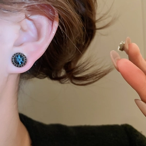 Detail view of a vintage round blue crystal stud earring worn on an ear showing size and style