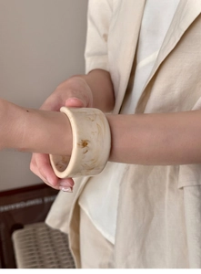 Detail of wide cream marble resin bangle showing smooth texture and amber stone patterns