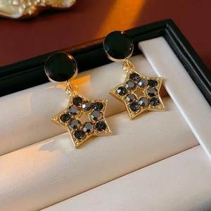 Gros plan détaillé des boucles d'oreilles étoile dorées avec strass noirs en écrin blanc