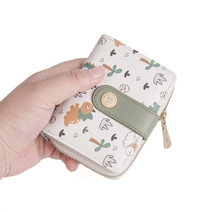 Close-up of cream short wallet featuring cartoon dinosaur print and gold snap button