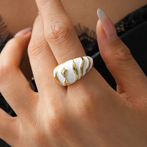 Chic gold spiral open ring with white enamel stripes worn by a model in a close-up shot