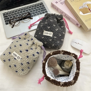 Plush heart drawstring makeup bags in grey, beige, and brown on a cozy desk setup