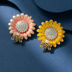 Detail of enamel sunflower and bee brooches with rhinestones on a blue textured background