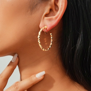 Side view of model wearing large gold twisted geometric faceted hoop clip-on earrings