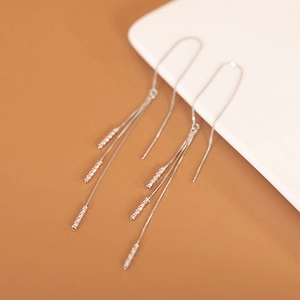 Macro detail of silver tassel earrings with multiple chains on a minimalist background