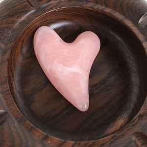 Pink resin heart-shaped facial massage tool with marble pattern in a carved wooden bowl