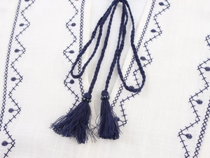 Close-up of white cotton linen shirt with navy blue embroidery and woven tassel ties