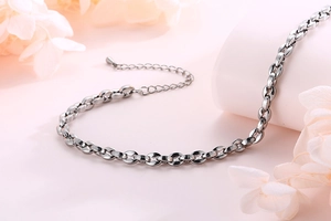 Detail einer silbernen Edelstahl-Fußkette mit Tropfenanhänger auf blumigem Hintergrund