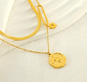 Detail of double-layer gold necklace featuring starburst pendant on off-white fabric