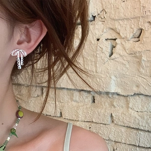 Gros plan d'une boucle d'oreille nœud en argent avec motif dentelle portée par un modèle