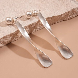 Detail of twisted matte silver metal earrings with faux pearl on a beige stone