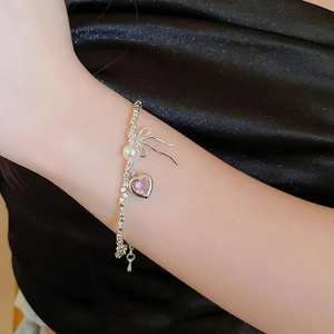 Detail of silver beaded bracelet featuring white pearl, pink heart gemstone, and bow charm